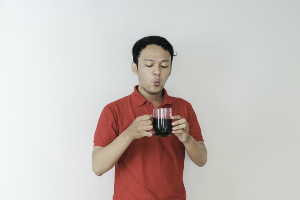 年轻的亚洲男子拿着一杯咖啡站在孤立的白色背景与震惊和哇表情图片下载