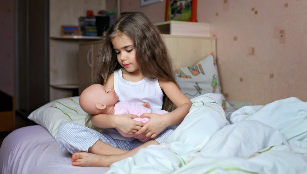 长头发的漂亮女孩在床上玩洋娃娃图片下载