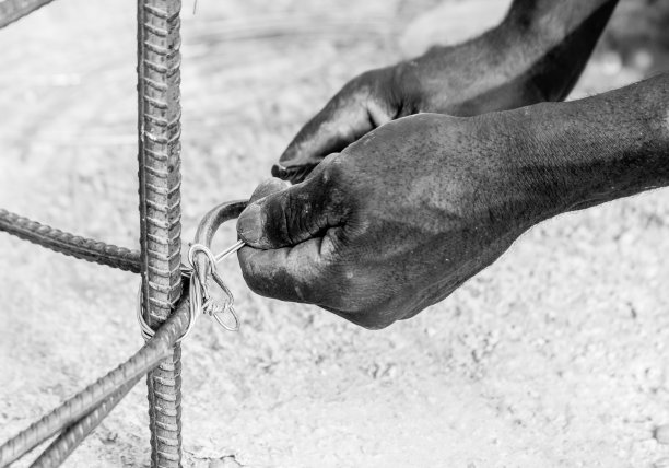 一名海地建筑工人将钢筋绑在柱子上准备用混凝土浇筑的黑白图像具有戏剧性的高对比度。图片下载