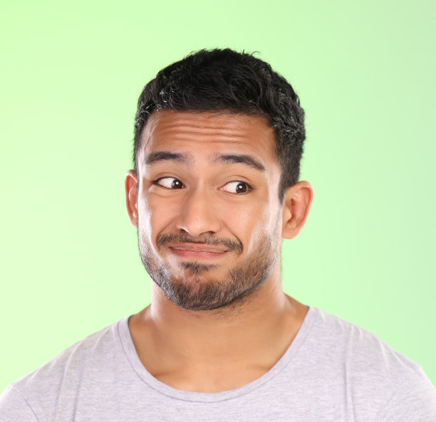 一个英俊的年轻人在工作室的绿色背景下做鬼脸的裁剪镜头图片下载