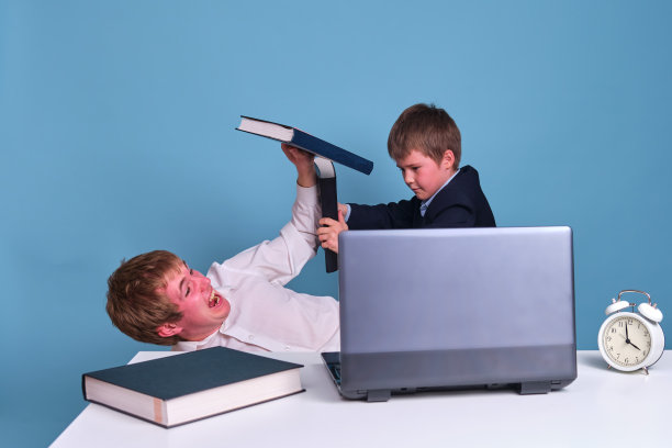 父子俩正用一台电脑在桌子的背景上用课本打架。冠状病毒流行期间的远程办公和研究问题图片下载