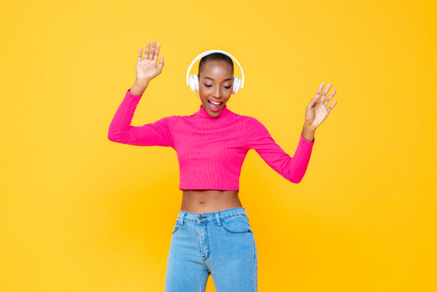 快乐的非洲裔美国妇女戴着耳机听音乐和跳舞在多彩的黄色孤立的背景图片下载