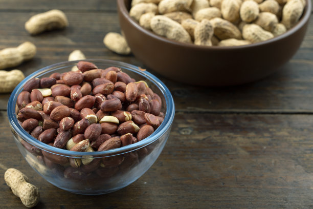 玻璃碗里有带壳的花生，桌上有带皮的花生。空间的文本。图片下载
