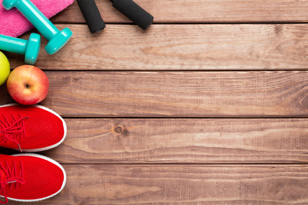 健身和运动概念。红色的运动鞋，苹果，跳绳，哑铃和粉红色的毛巾在木制的背景上。自由空间图片下载