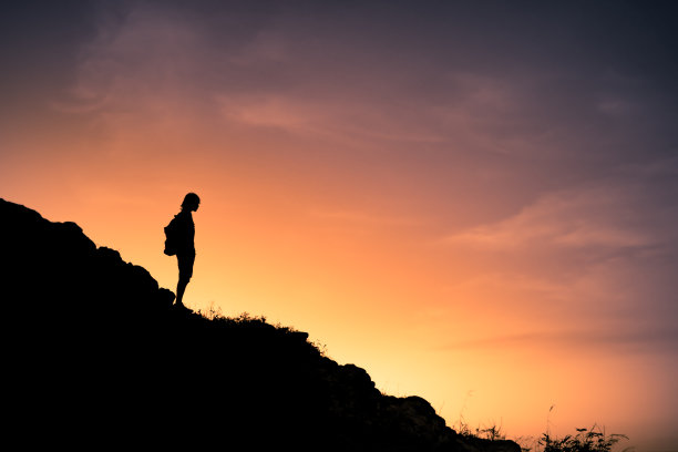 面对日落，站在山边的徒步者的剪影。图片下载