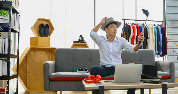 一位亚洲男子在博客上播放一段视频，介绍他在网上销售帽子、鞋子、耳机、衣服、安全头饰等产品。在家购物的概念图片下载