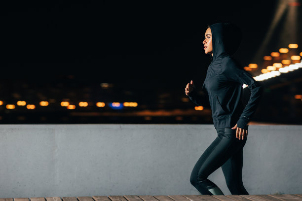 年轻女性慢跑者在夜间户外锻炼的侧视图。沿着堤岸跑的女人。图片下载