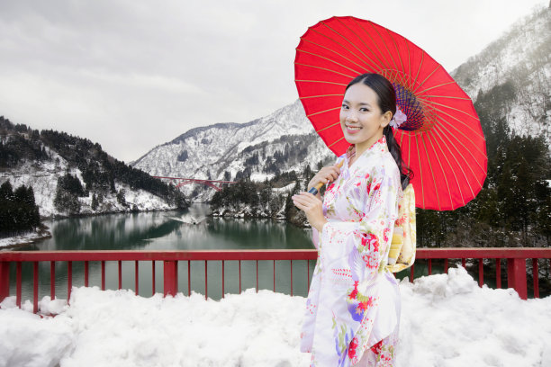一个穿着和服的年轻女子，拿着一把红伞，站在有雪和船的桥上。富山位于日本。图片下载