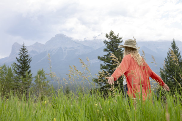 戴着太阳帽的成熟女人享受着郁郁葱葱的山间草地图片下载