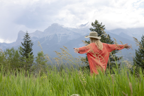 戴着太阳帽的成熟女人享受着郁郁葱葱的山间草地图片下载