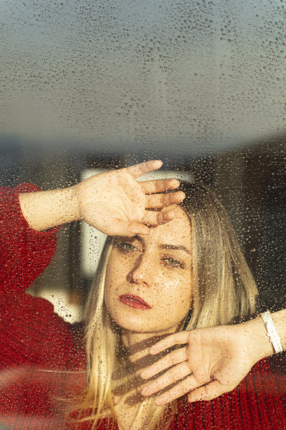 金发女人看起来悲伤和沮丧。一名年轻女子双手压在玻璃上，望着被雨淋透的窗户。用于拷贝空间的空间。图片下载