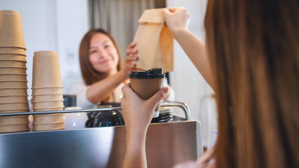 在一家商店里，拿着咖啡和装在纸袋里的外卖食品给顾客的女服务员图片下载