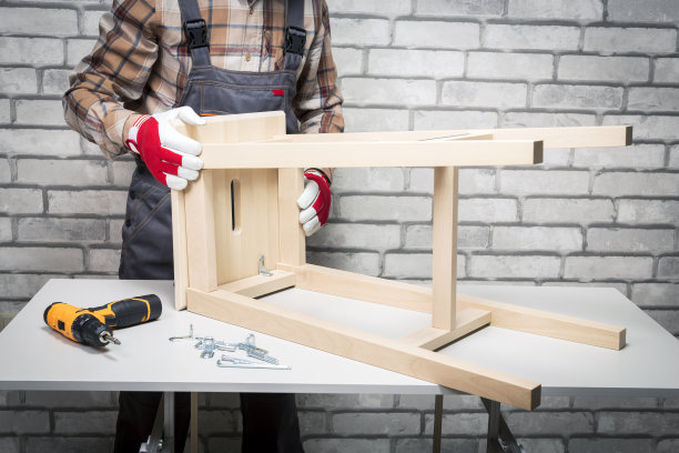 穿着制服的男子在家里组装木椅家具。组装家具服务。图片下载