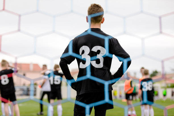 高个少年守门员站在球门上。模糊前景中的足球球门网。小男孩在足球手套玩游戏作为一个守门员图片下载