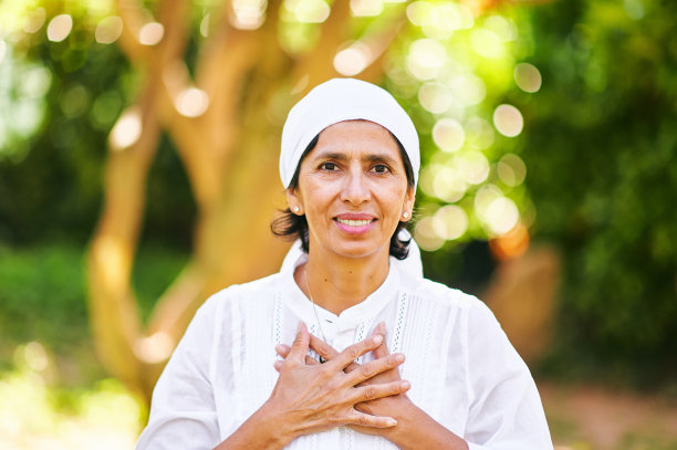 户外肖像成熟的女人休息在阳光灿烂的公园或花园，手牵手在胸前，感激的标志图片下载