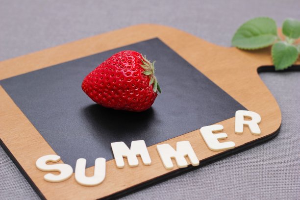 一个成熟的鲜红草莓放在木砧板上，旁边用木制字母写着“夏天”。图片下载