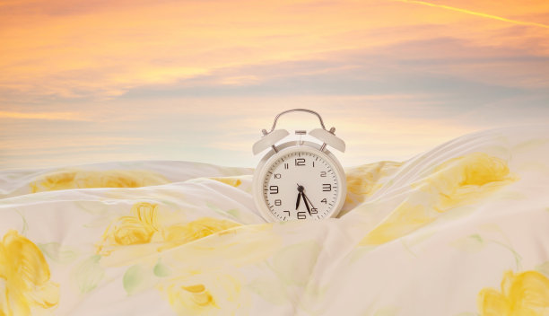 床上的钟。闹钟上的羽绒被，枕头与日出-黎明天空的背景在早上。广告的概念图片下载