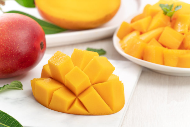 将新鲜的芒果切成小块，放在带有叶子的白色盘子里。图片下载