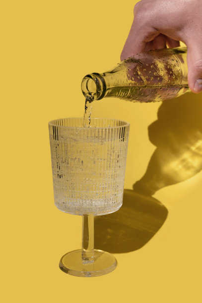 一名男子用手将水倒在玻璃上，背景为黄色，有日出日落的阴影。时髦的最小概念。图片下载