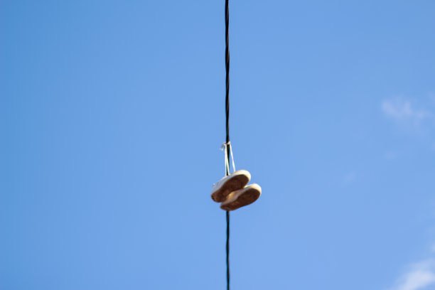 离焦运动鞋脚挂在电线上，以蓝色的天空为背景。城市文化的概念，违禁物品的销售，贫民窟。水平的照片。特写镜头。的焦点图片下载