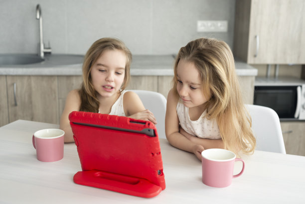 两姐妹在现代厨房的平板电脑上看有趣的视频。在线教育或家庭时间的概念图片下载