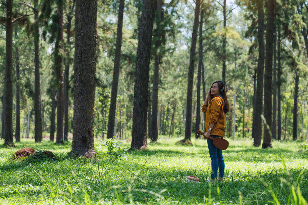 一个女人拿着四弦琴，戴着耳机在公园里听音乐图片下载