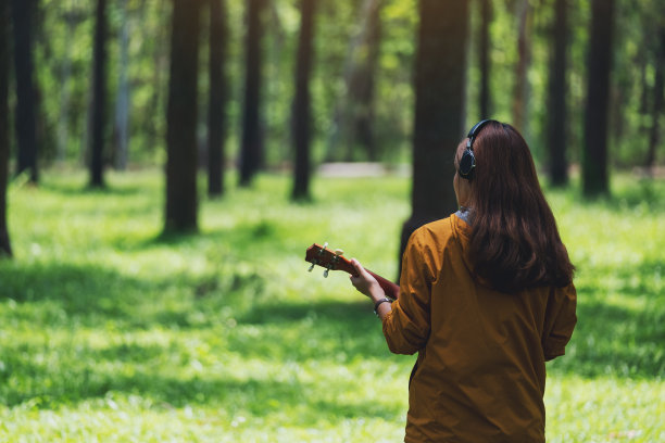 一位女士喜欢在公园里边听音乐边玩尤克里里琴图片下载