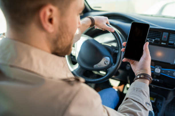 手持智能手机开车的男人。男性一边开车一边看手机屏幕图片下载