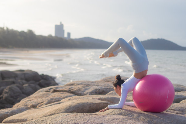 年轻迷人的亚洲女人练习瑜伽与瑜伽球在海滩上。图片下载