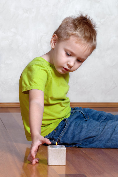 漂亮而严肃的金发小白种人男孩坐在地板上点燃蜡烛。图片下载