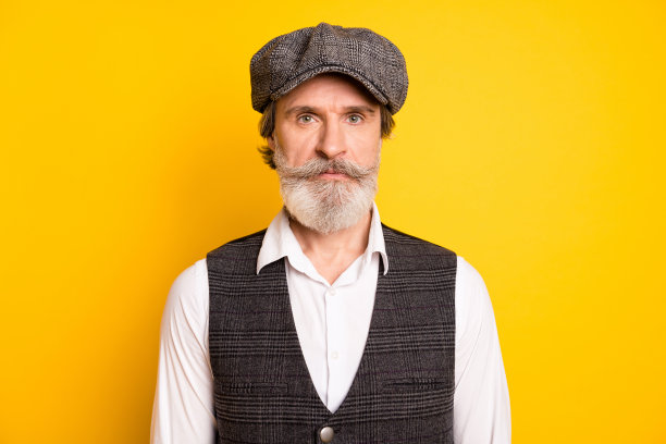 照片上的老帅哥绅士严肃自信穿背心，帽子孤立在黄色背景图片下载