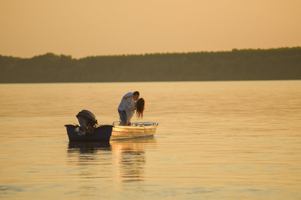 年轻的情侣在河上的船上接吻。黄金时间日落照片。图片下载