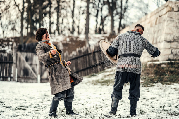 两个身穿盔甲，手持武器的古代战士在雪地里用剑搏斗图片下载