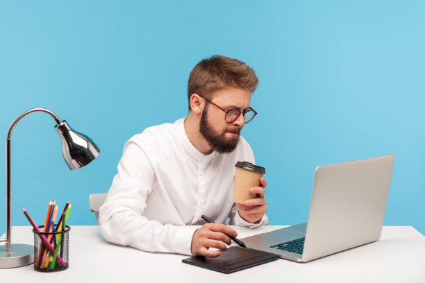 忙碌而专注的创意设计师坐在工作场所，一边工作一边喝着咖啡，认真地看着笔记本电脑的显示屏图片下载