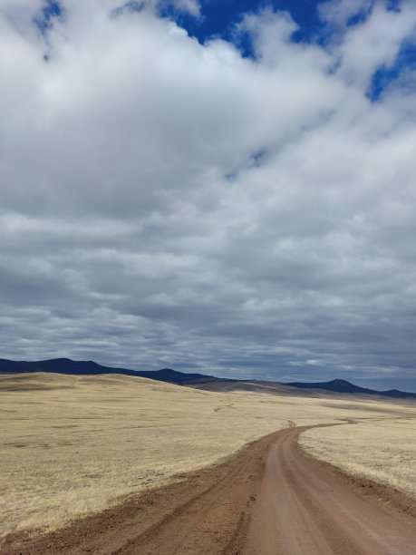 乡村土路穿过草原山谷与黄色的干草和山在地平线下阴天图片下载