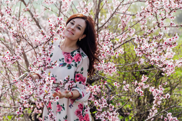 美丽的黑发女人穿着一件连衣裙，带着鲜花走过春天的花园图片下载