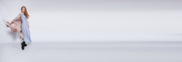 美丽的女孩在米色雨衣摆姿势在工作室在灰色的背景图片下载