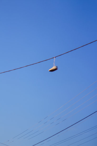 在蓝色的天空背景下，把挂在电线上的运动鞋散焦。城市文化的概念，违禁物品的销售，贫民窟。垂直的摄影。的焦点图片下载