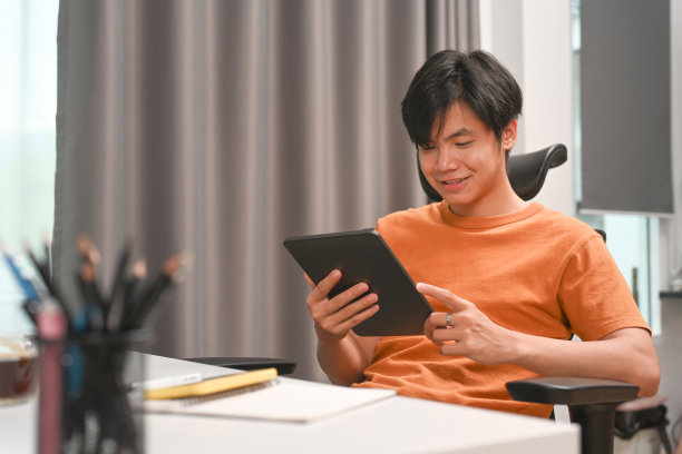 快乐的年轻自由职业者坐在家庭办公室的椅子上，使用数字平板电脑。图片下载