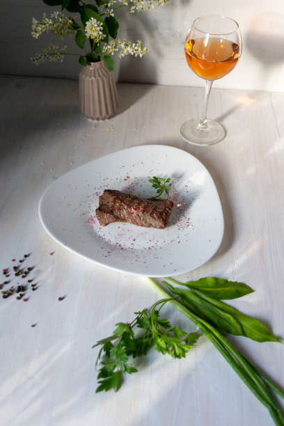 带血的半生不熟的牛排，配以香料，玫瑰酒，绿叶菜和鲜花图片下载