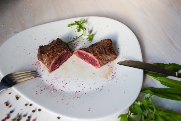 鲜嫩多汁的带血牛排，用刀叉切开，盛在配有香料、玫瑰酒、绿叶植物和鲜花的白盘子里图片下载