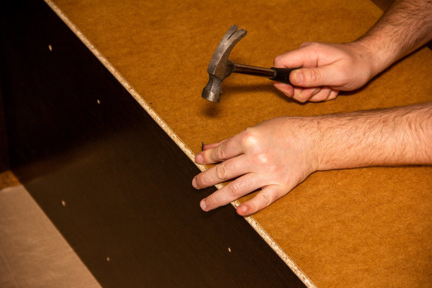 一个木匠家具制造者用锤子把一颗钉子钉进橱柜的后面图片下载
