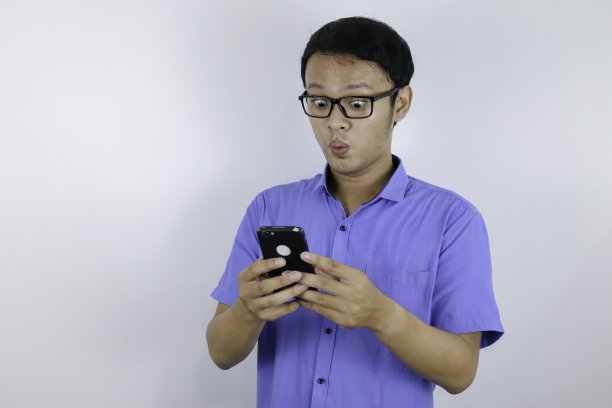 年轻的亚洲男子震惊和快乐时，他看智能手机图片下载