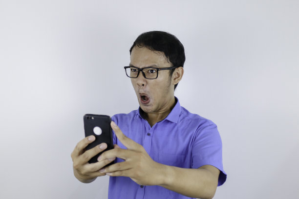 年轻的亚洲男子震惊和快乐时，他看智能手机图片下载