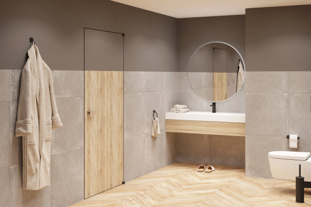 现代浴室，灰色的墙壁和木地板，洗脸盆上方有一面圆形镜子，上面有一个木制的橱柜，一间厕所，门附近有一件浴衣，天花板上有射灯。图片下载