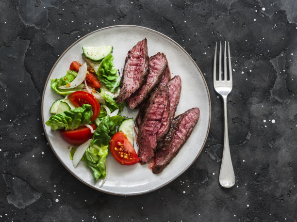 美味的午餐-生菜，黄瓜，西红柿沙拉和牛排在一个黑暗的背景，俯视图图片下载