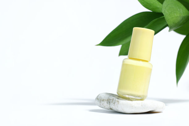 创意模型的孤立化妆品瓶与黄色指甲油与植物，在石头上，在白色背景与植物的硬阴影。指甲护理、美甲或足疗的概念。横幅图片下载