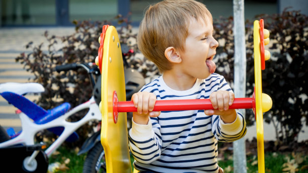 有趣的小男孩的肖像骑在儿童游乐场和显示舌头图片下载