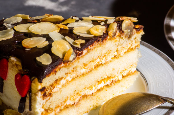 一块多层的自制海绵蛋糕，放在白色的托盘上，配上勺子和亚麻餐巾，黑色背景，强光，低调拍照。图片下载