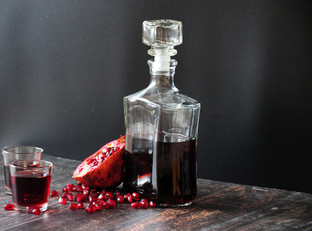 黑墙边的木桌上放着一瓶石榴甜酒，两杯，熟透的水果和种子。图片下载